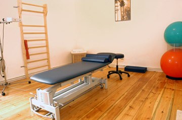 Behandlungszimmer der Praxis: blaue Therapieliege auf Altbaudielen,
                        daneben eine Sprossenwand.